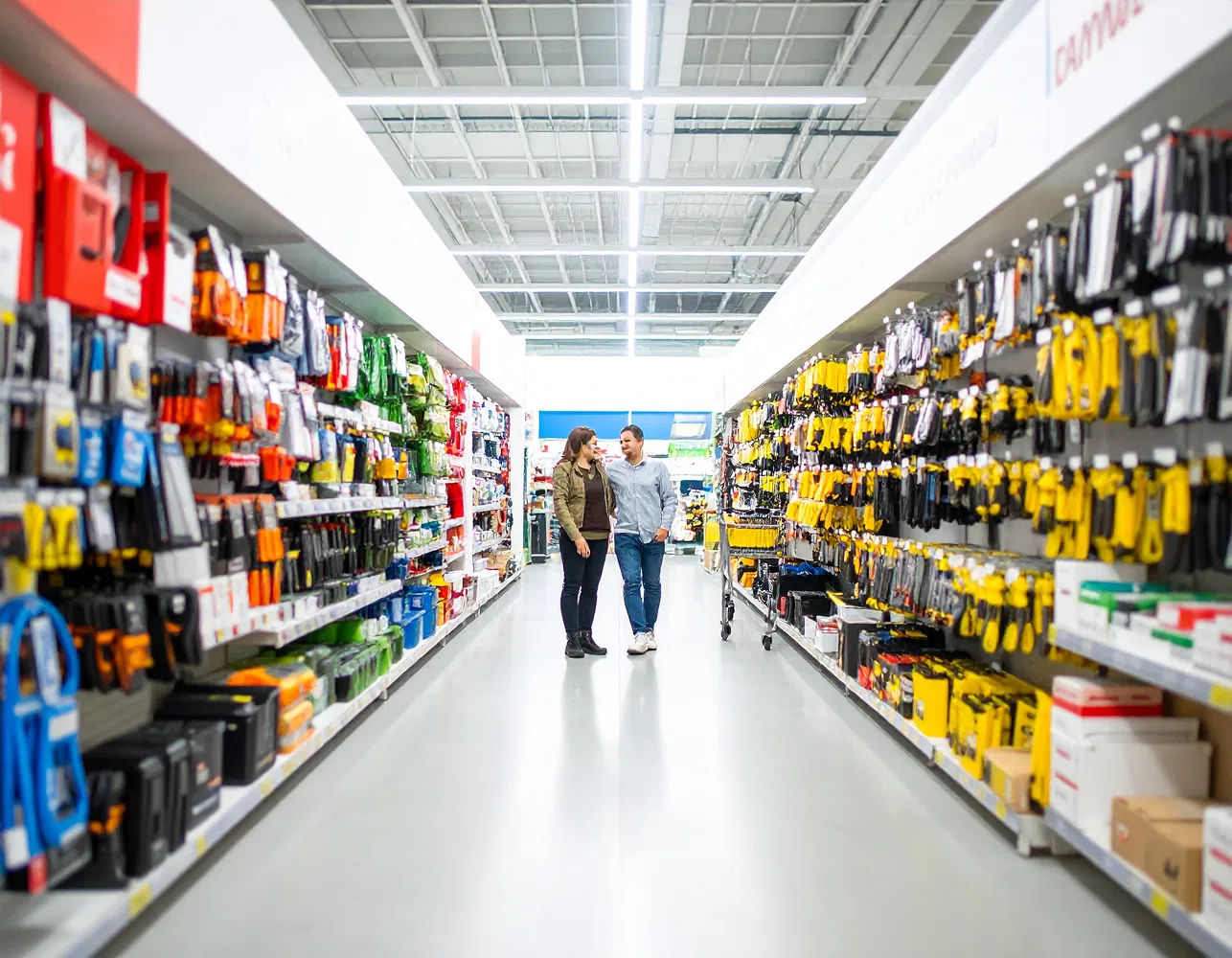 shop-in-shop-baumarkt Paar steht in einem Gang eines Baumarkts, links und rechts Regale voller Werkzeuge und Zubehör.