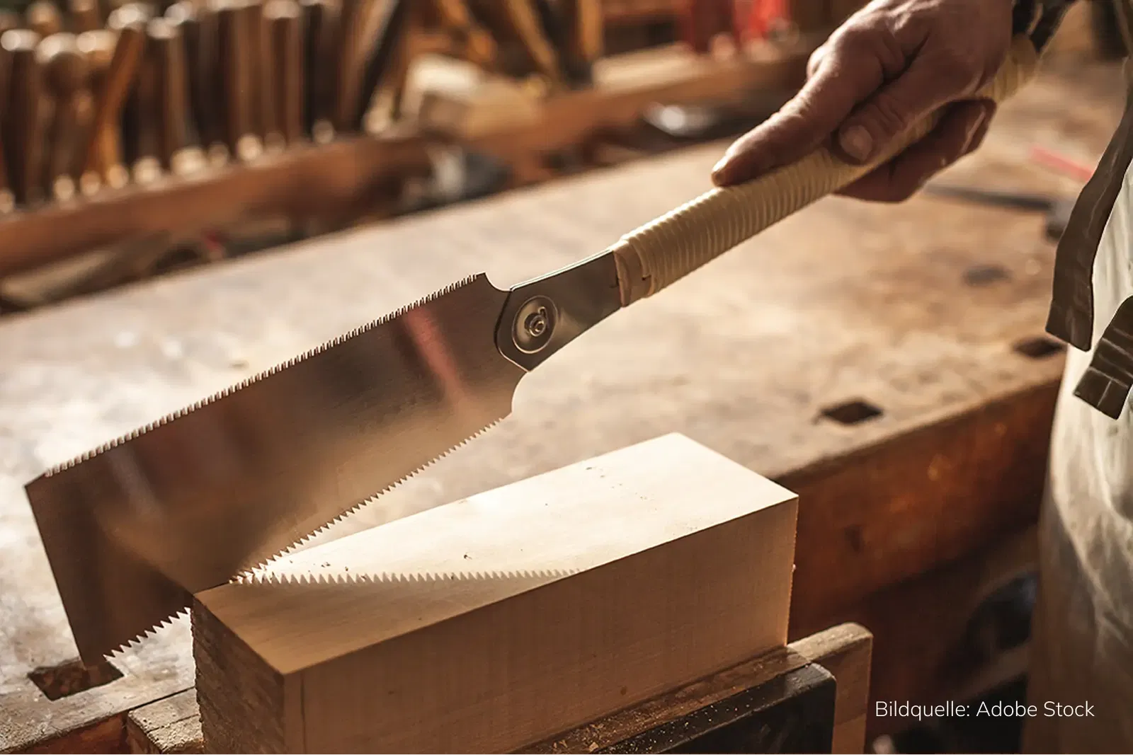 B2B-Werkzeughandel Success Story Handwerker schneidet mit einer japanischen Zugsäge ein Stück Holz auf einer Werkbank in einer traditionellen Holzwerkstatt.
