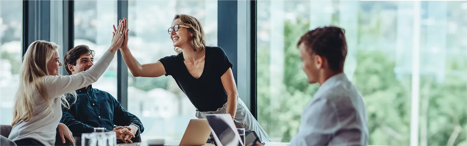 Mehr über elio erfahren Bussiness-Situation: Vier Personen sitzen in einem Meetingraum und zwei davon klatschen sich mit den Händen gegenseitig ab.