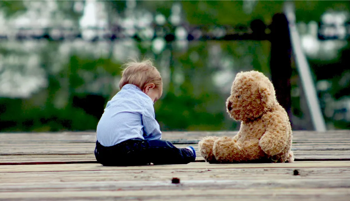 Kinder- und Jugendhospiz „Kleine Helden“ Osthessen e.V. Ein Bild von einem kleinen Kind, das neben seinem Teddybären sitzt.