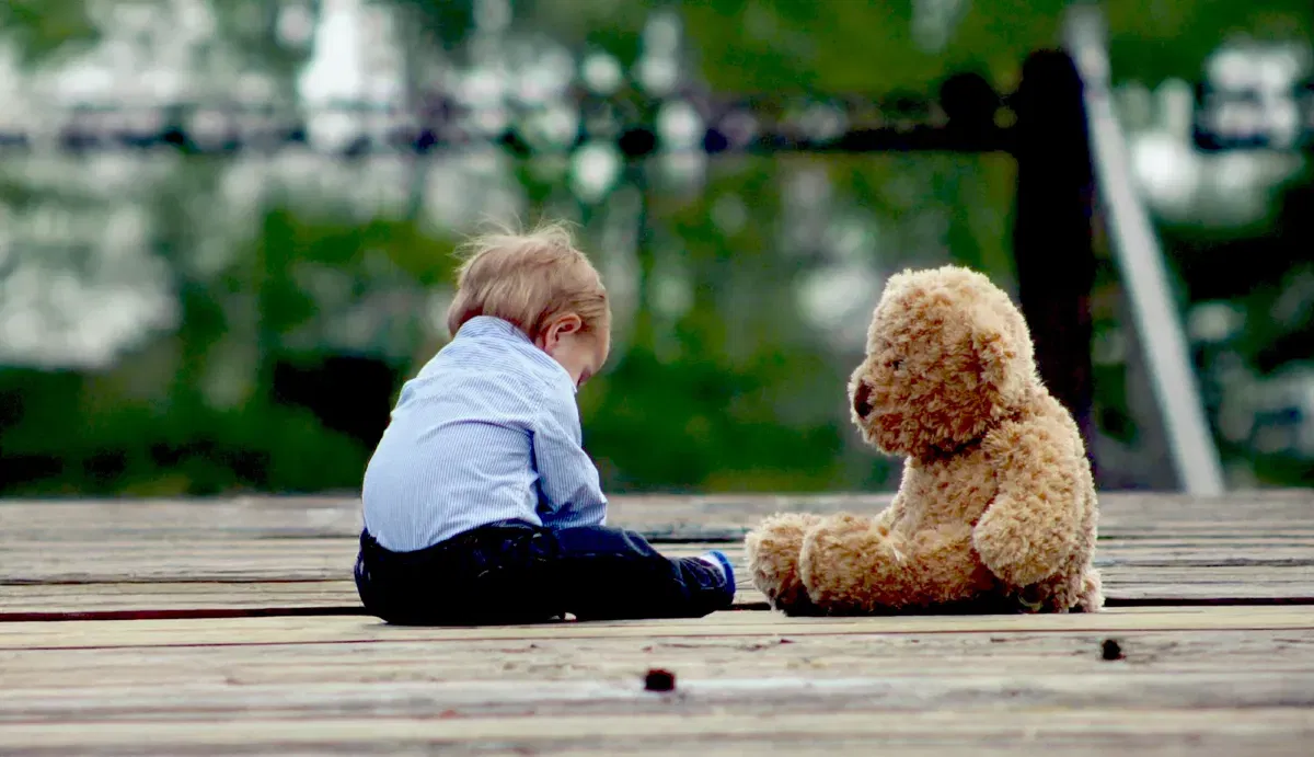 Kinder- und Jugendhospiz „Kleine Helden“ Osthessen e.V. Ein Bild von einem kleinen Kind, das neben seinem Teddybären sitzt.