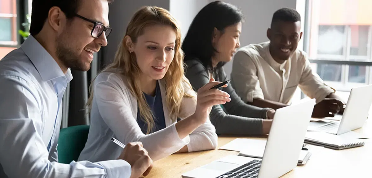 Training für Anwender Gruppe von Mitarbeiter:innen am Arbeitsplatz vor Laptops, die miteinander kommunizieren