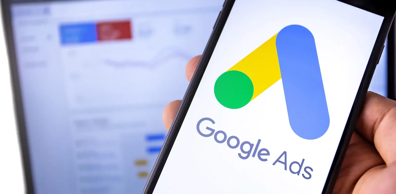 Google Ads Smartphone mit geöffnetem Google Ads Logo, im Hintergrund unscharfer Bildschirm mit Analytics-Dashboard – Symbol für Online-Werbung und Performance-Marketing.